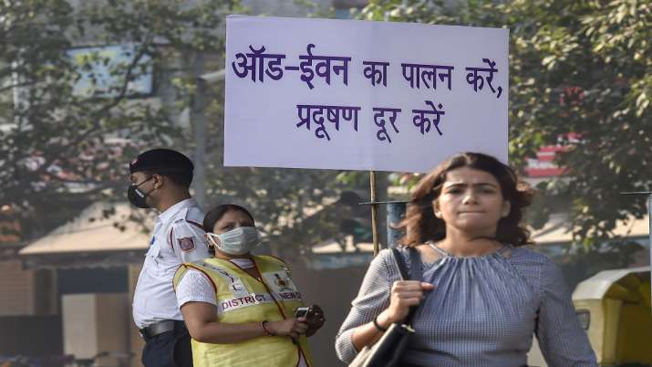 Civil Defence volunteer wearing a mask displays a placard asking people to obey the odd-even rule, i Civil Defence volunteer wearing a mask displays a placard asking people to obey the odd-even rule, i- India TV Paisa